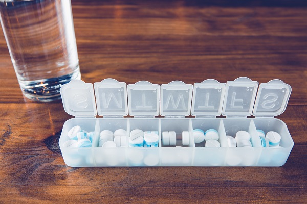 Tablets in a weekly container on a table with a glass of water